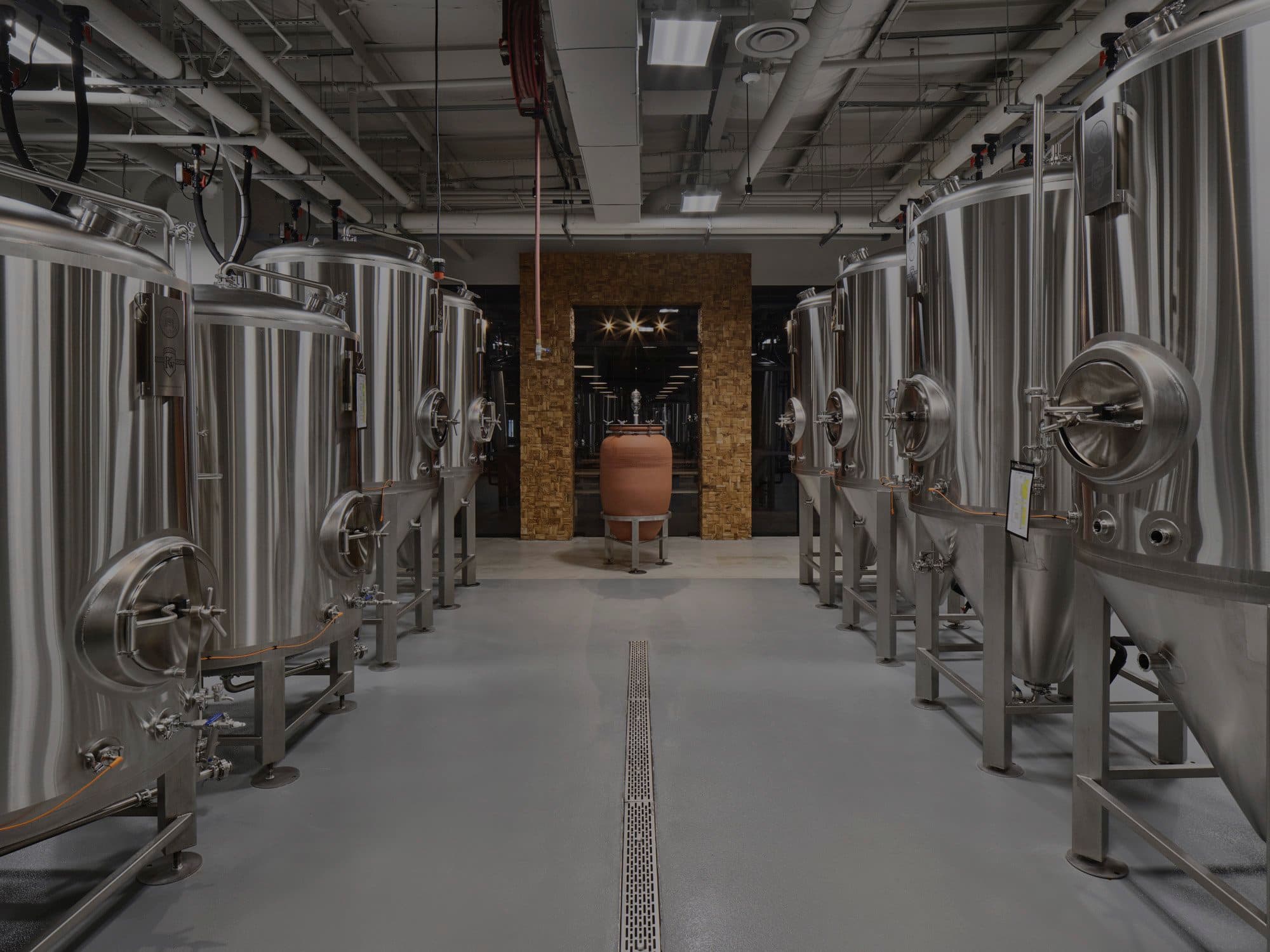 Stainless fermentation tanks lining the Deadwords brewhouse, with a clay amphora under a lit archway